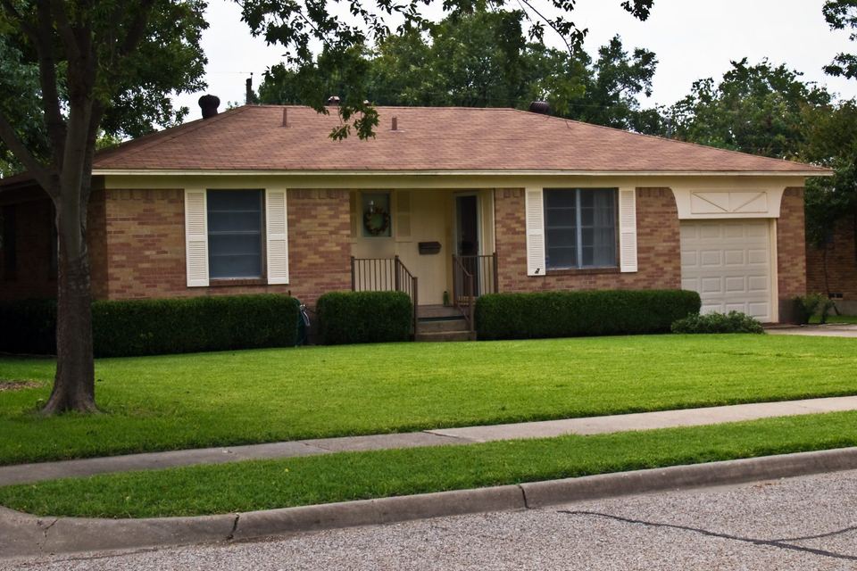 One-story brick ranch house with a brown shingle hip roof, white shutters and a front lawn